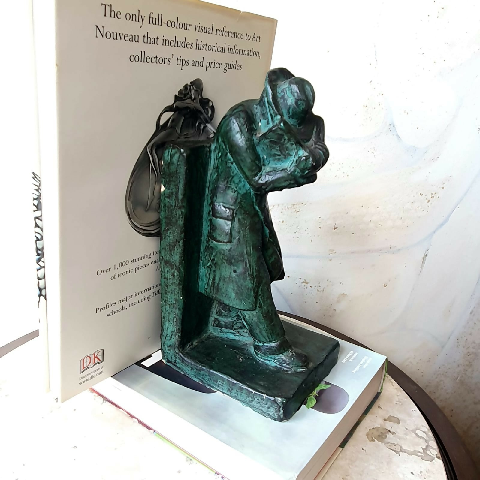 Escultura em cerâmica segura livros representando homem em momento de leitura