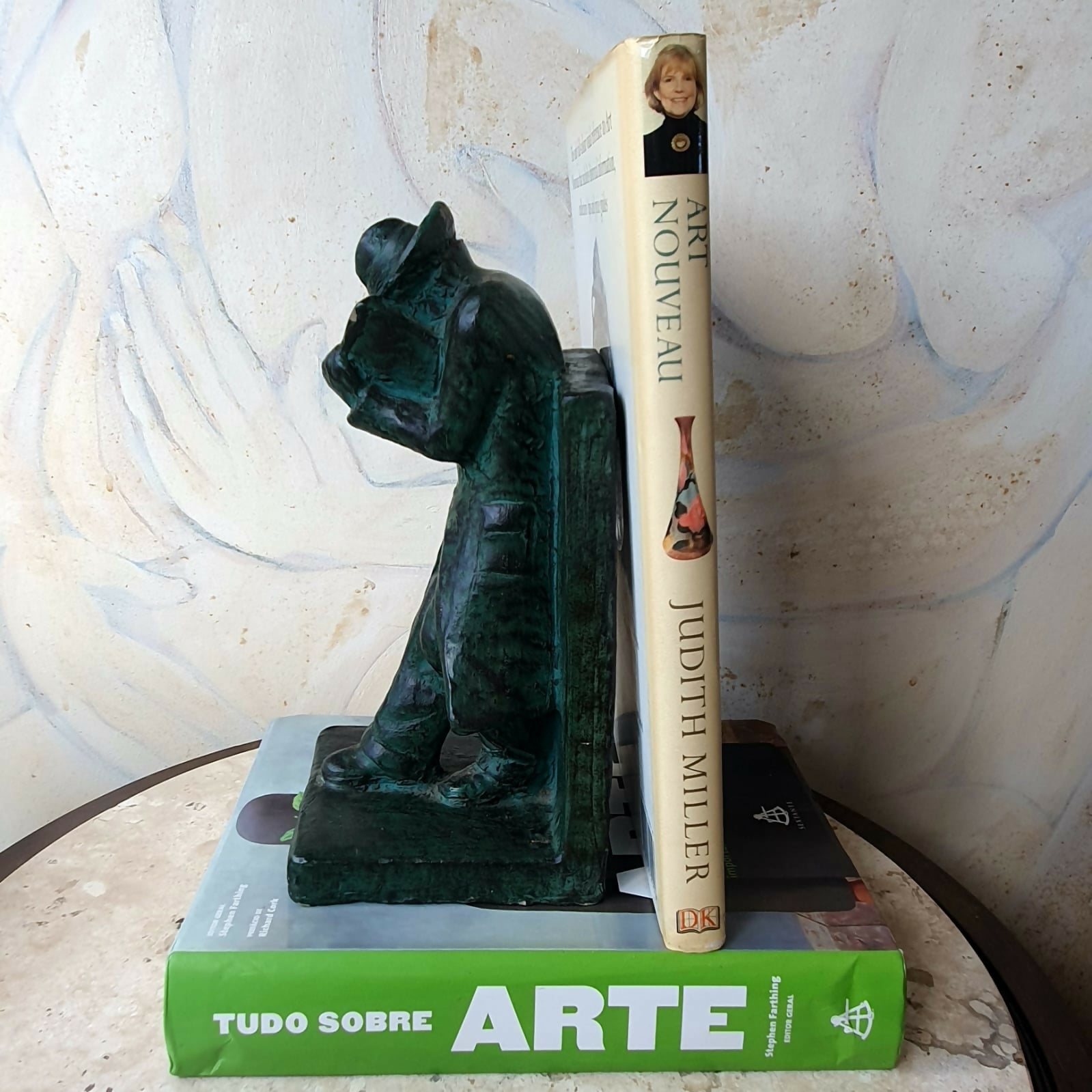 Escultura em cerâmica segura livros representando homem em momento de leitura