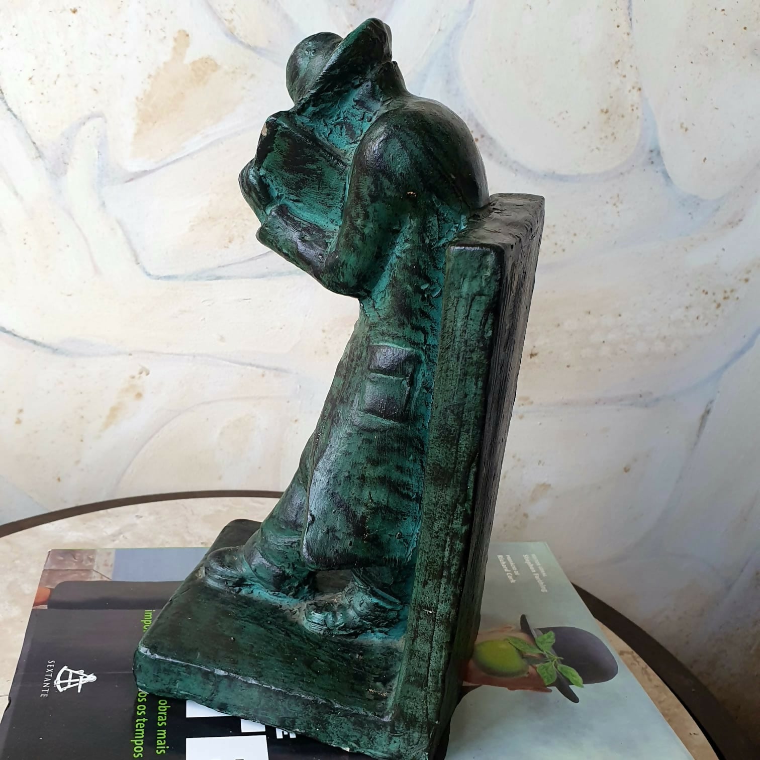 Escultura em cerâmica segura livros representando homem em momento de leitura