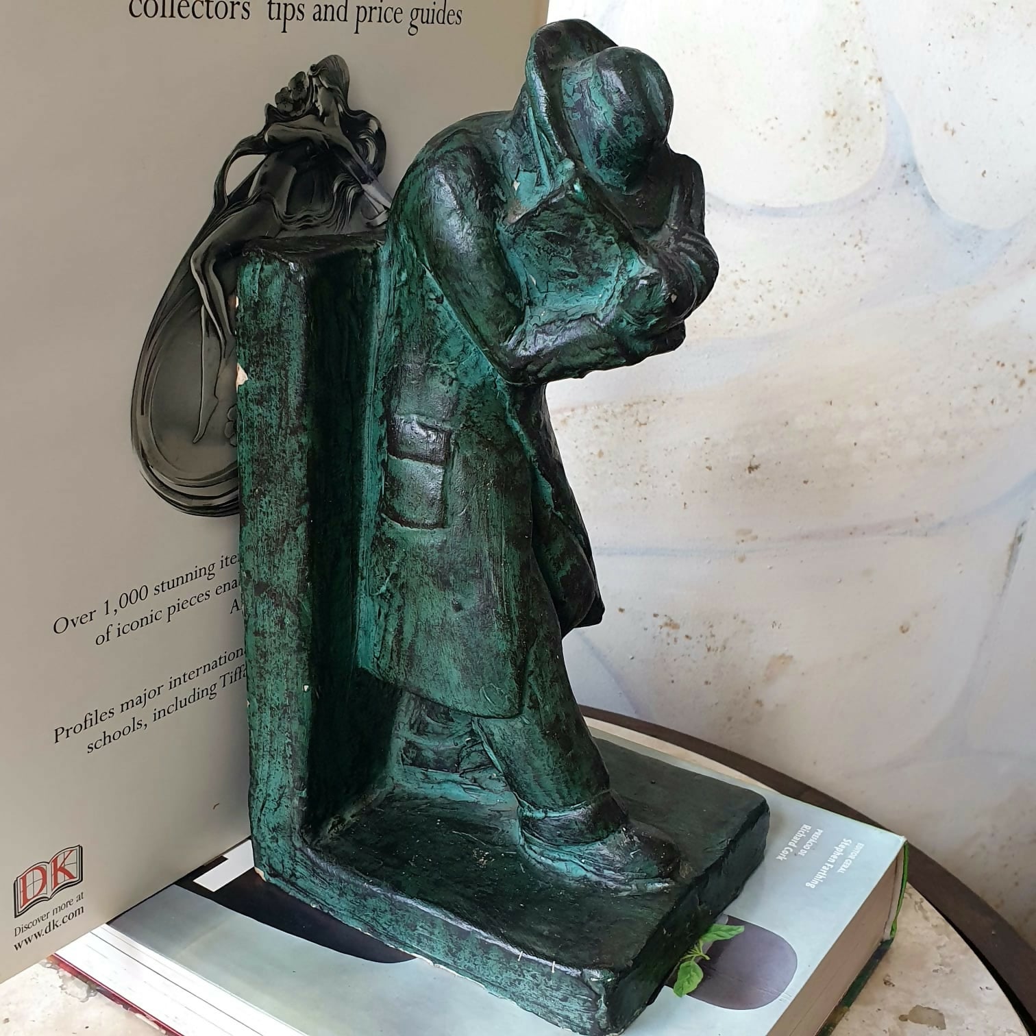 Escultura em cerâmica segura livros representando homem em momento de leitura