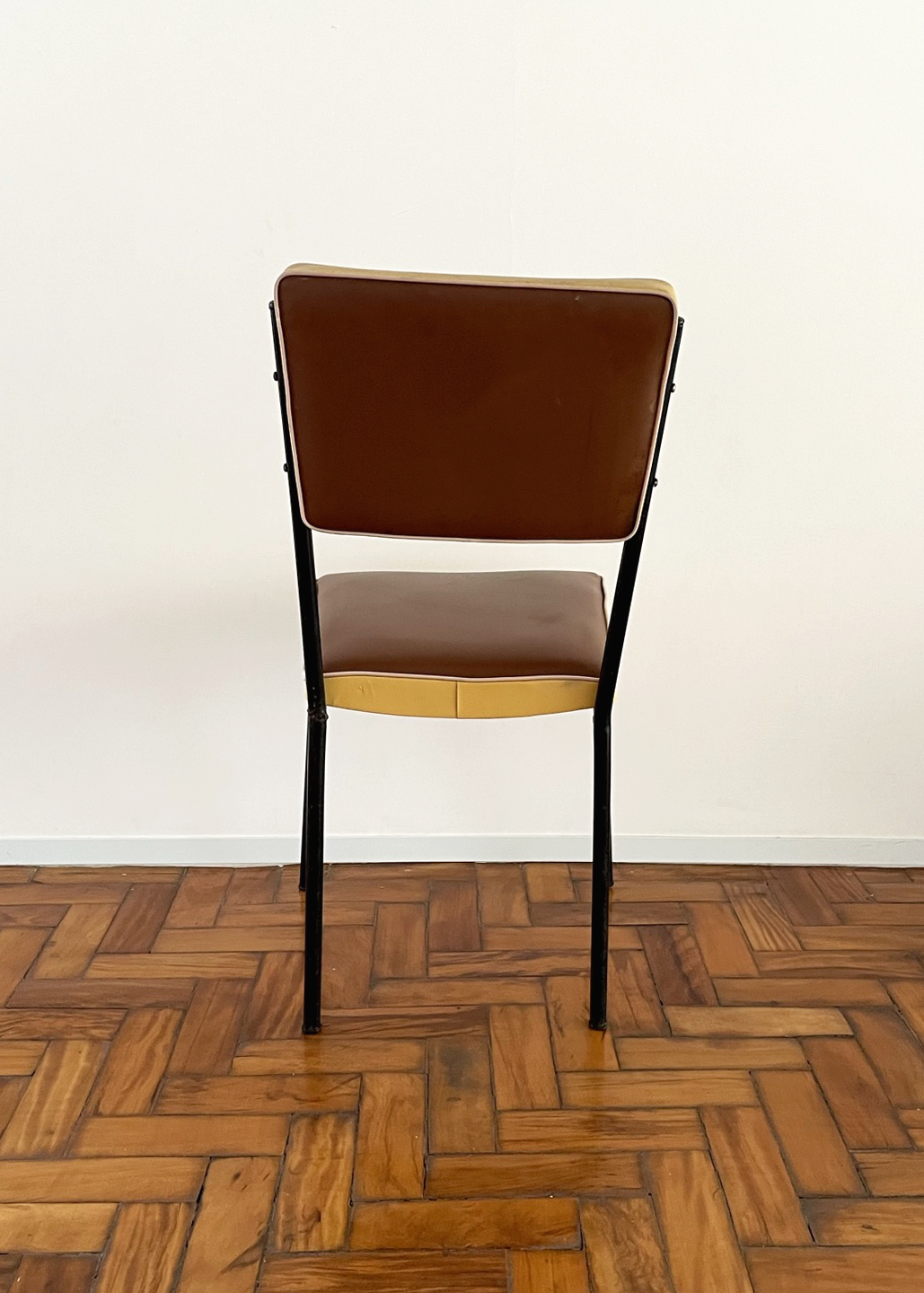 Cadeira cinquentinha. Estofado marrom, detalhe creme e estrutura metálica preta.