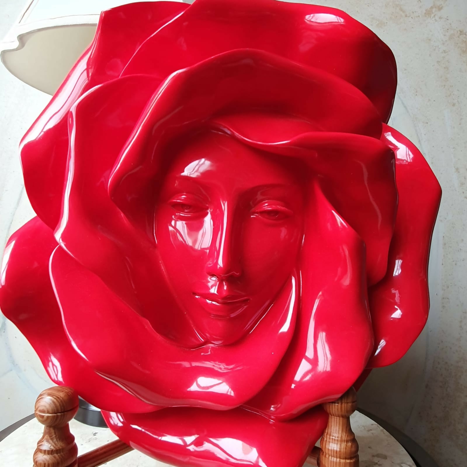 Escultura de parede em resina vermelha de rosto feminino envolto em pétalas de rosas.