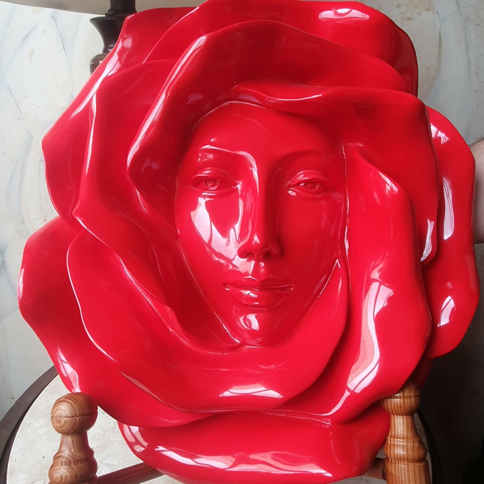Escultura de parede em resina vermelha de rosto feminino envolto em pétalas de rosas.