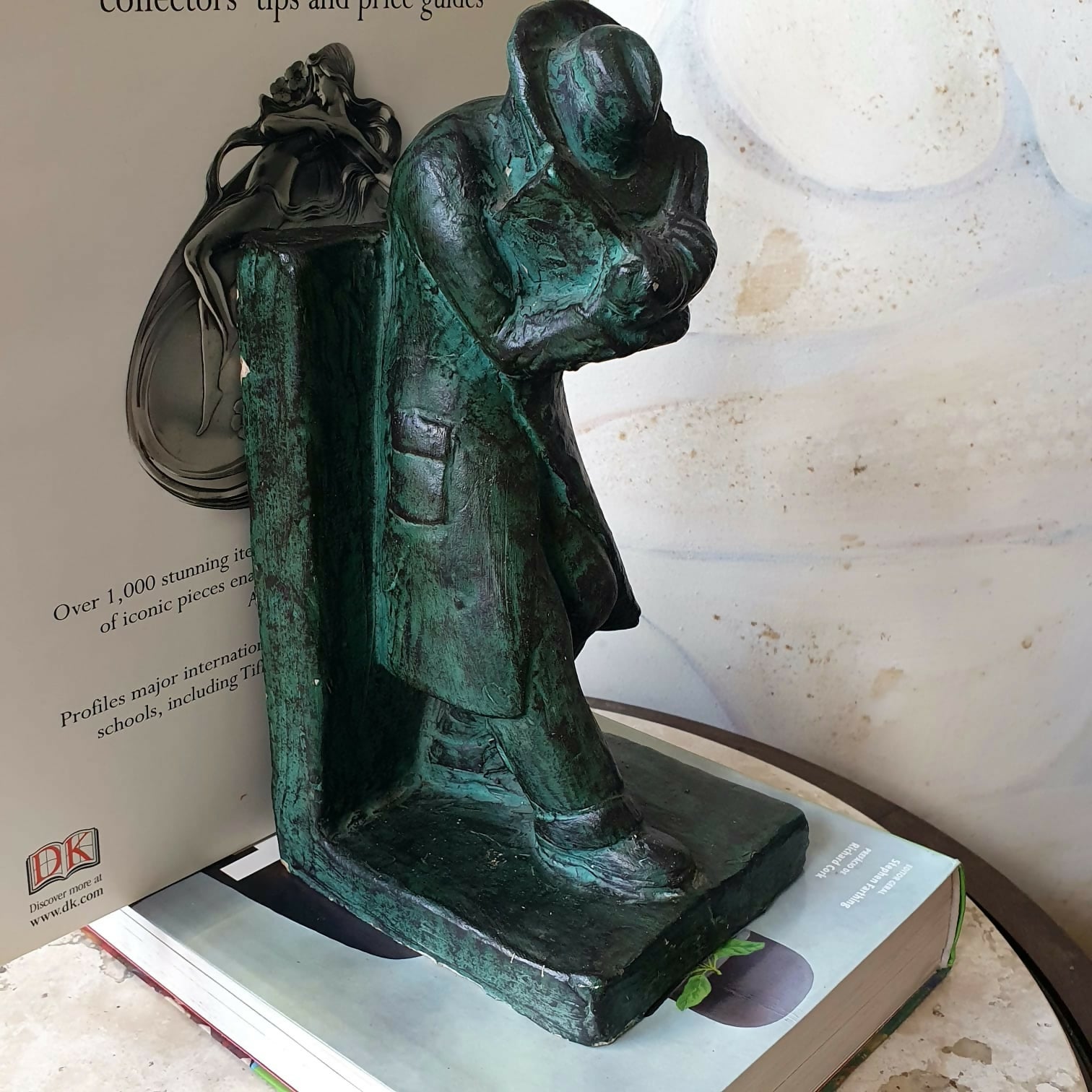 Escultura em cerâmica segura livros representando homem em momento de leitura