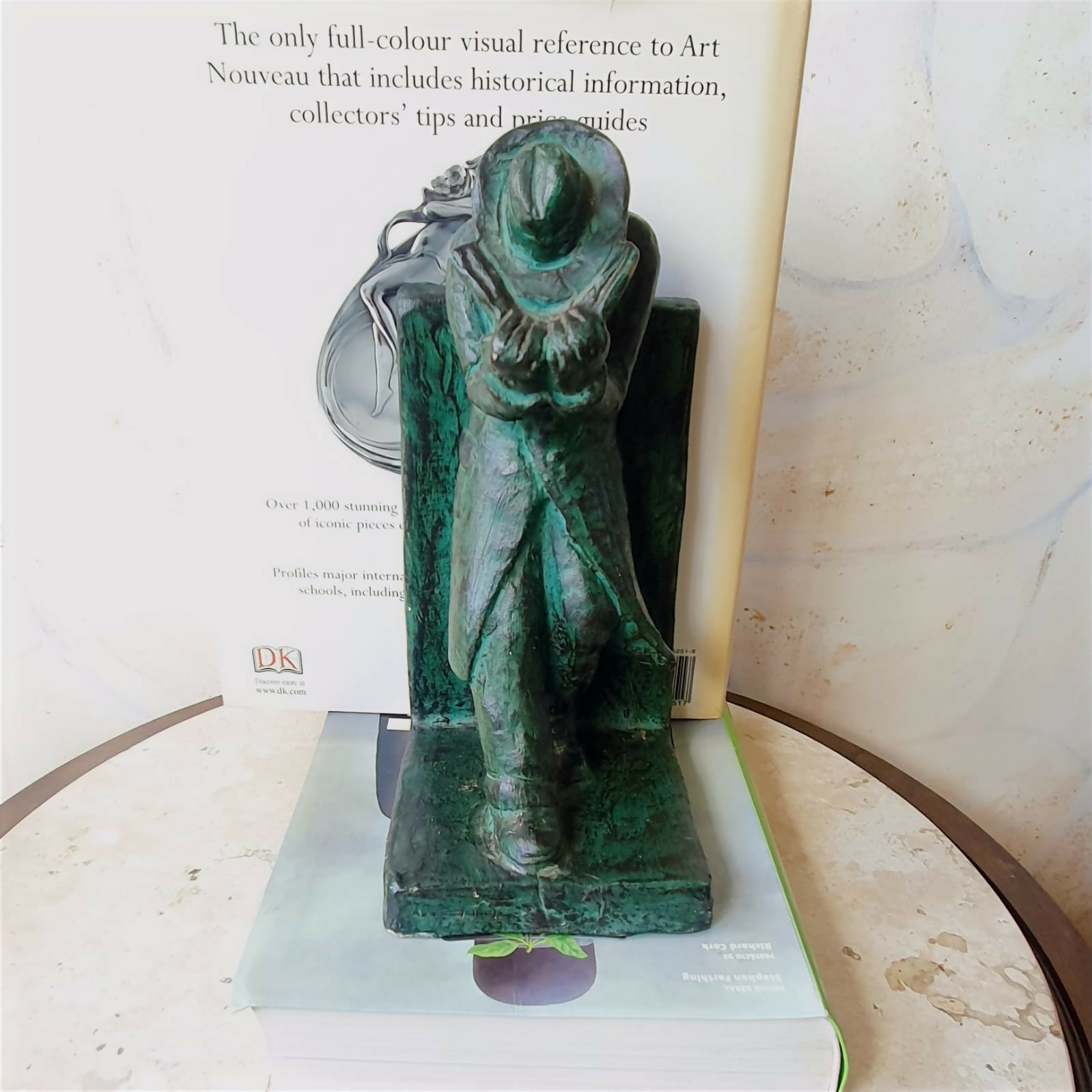 Escultura em cerâmica segura livros representando homem em momento de leitura