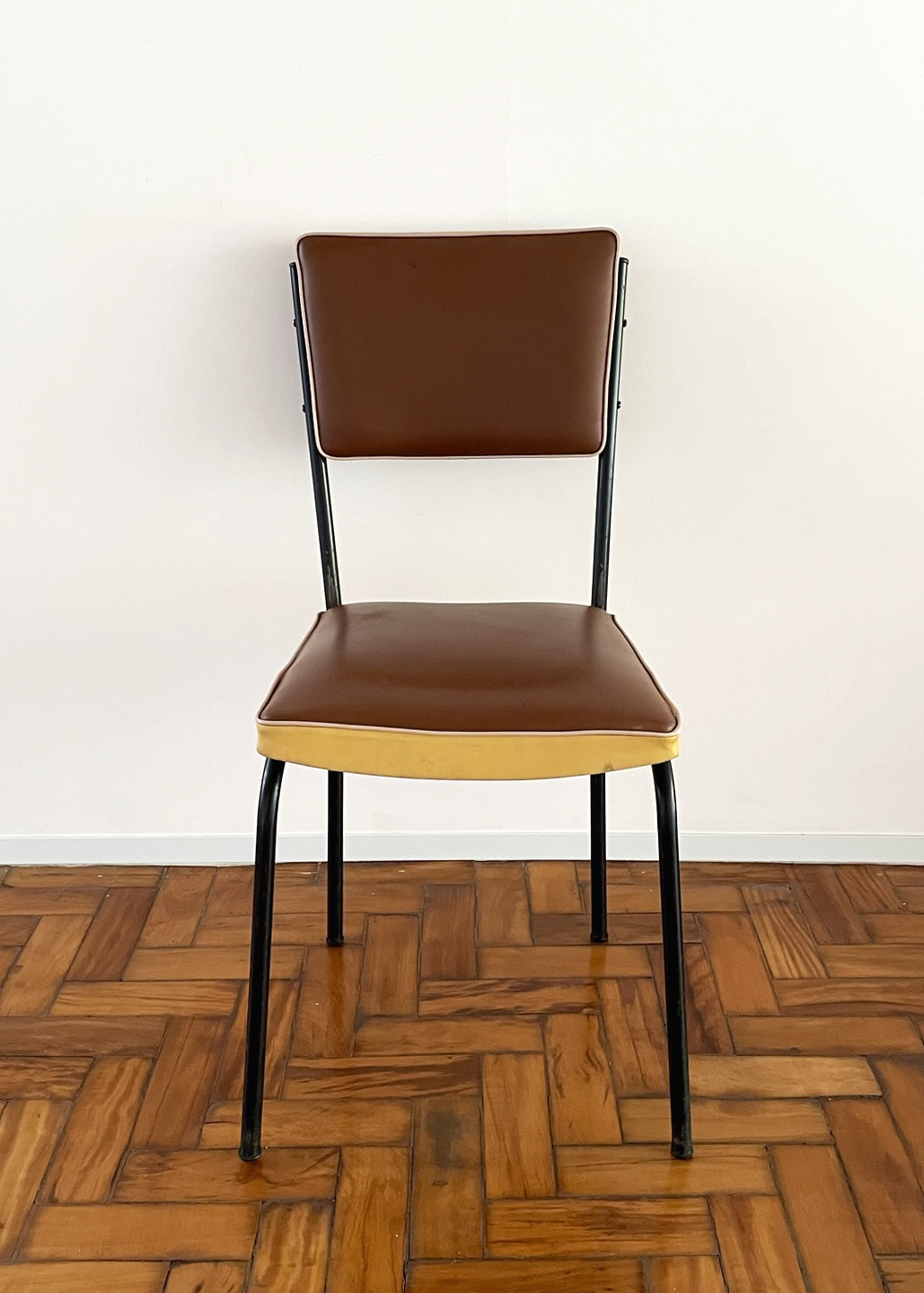 Cadeira cinquentinha. Estofado marrom, detalhe creme e estrutura metálica preta.