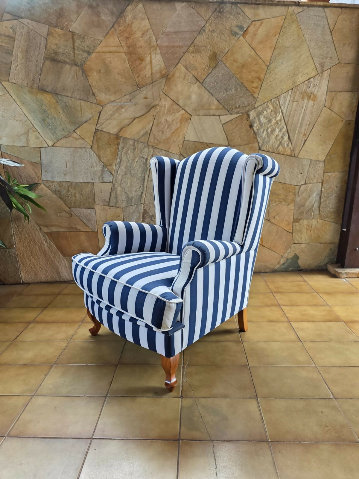 Poltrona bergere estofada e forrada com tecido acquablock listrado branco e azul.