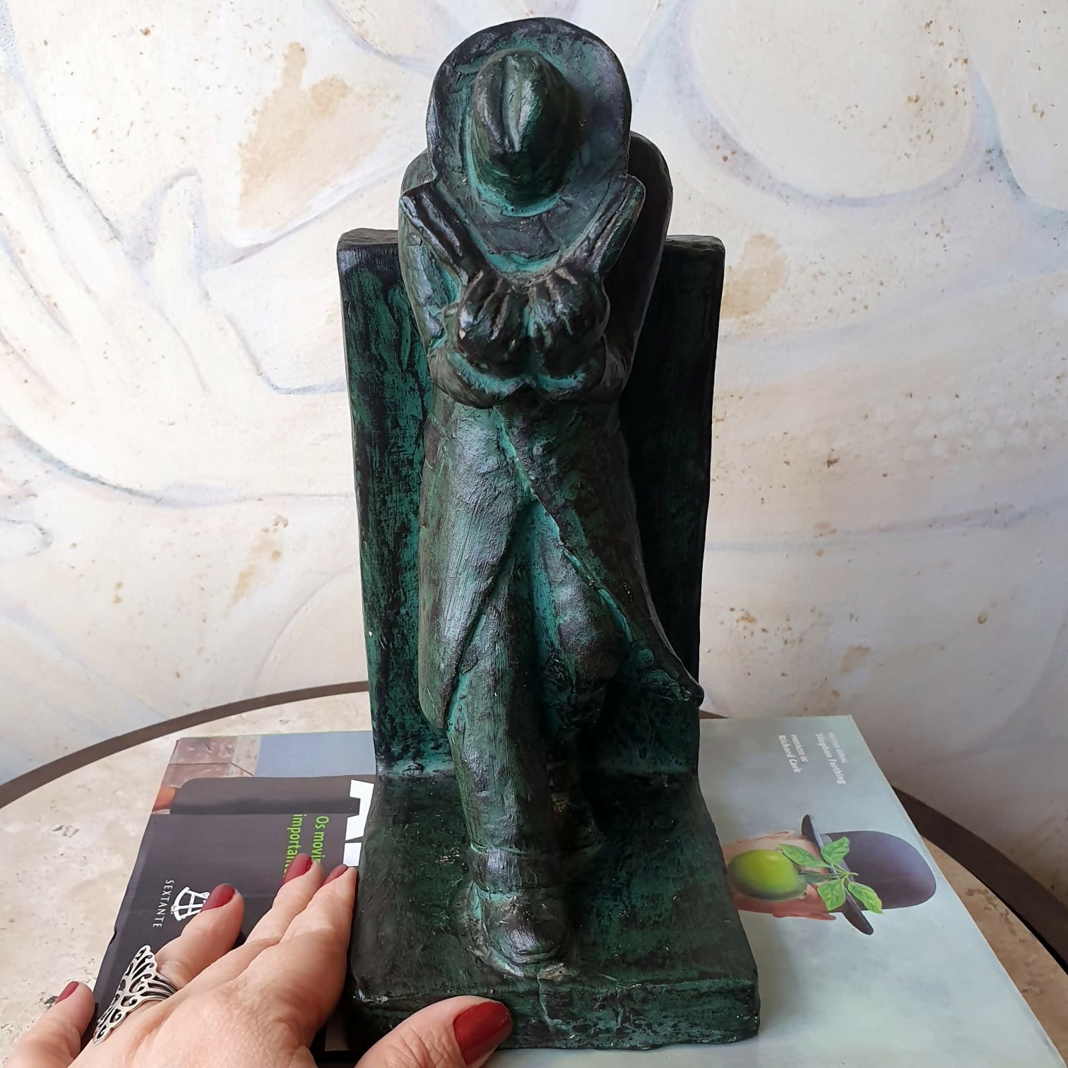 Escultura em cerâmica segura livros representando homem em momento de leitura